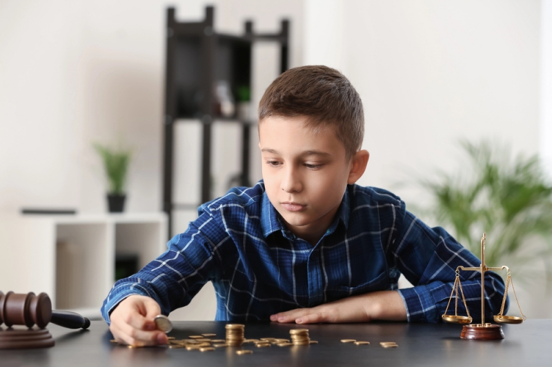 Chłopiec układający monety na stole obok młotka sędziowskiego - artykuł o tym co wpływa na wysokość alimentów na dziecko